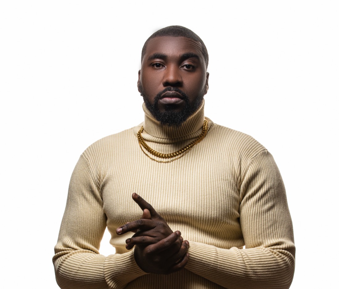 DJ OMG PRINCE in a cream turtleneck with gold chains against a white backdrop